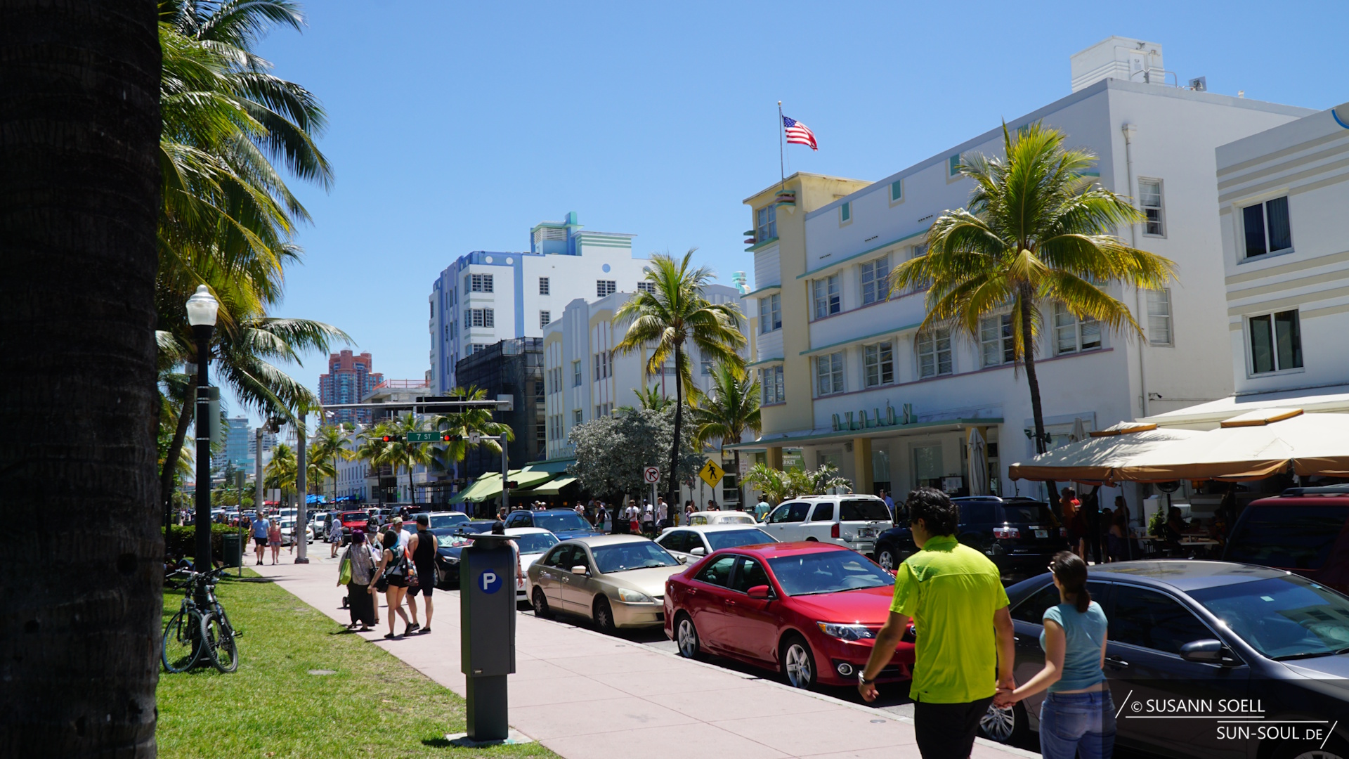 Hotelreihe am South Beach, die Straße ist voll mit geparkten Autos, sommerlich begleitete Menschen laufen auf dem Gehweg