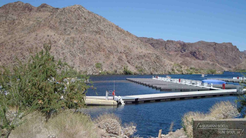 Über eine lange, schmale Zufahrt gelangt man zu einem blau-glitzernden See, an dessen Ufer niedliche, meckernde Ziegen grasen und die einzige Tanksäule weit und breit steht.